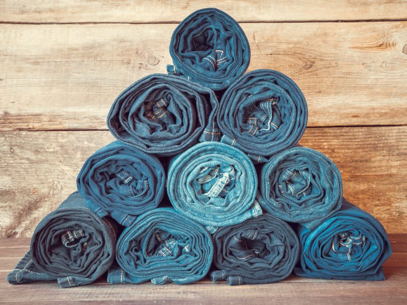 Rolled jeans stack on wooden background, retro toned.